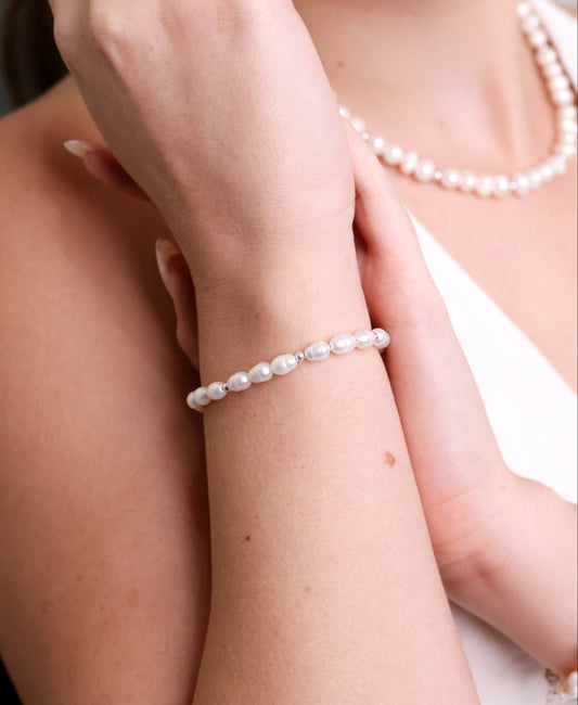 צמיד BELA BRACELET SILVER על פרק יד דוגמנית, מבט תקריב ממעלה על פנינים טבעיות וחרוזי כסף. ברקע שרשרת פנינים.