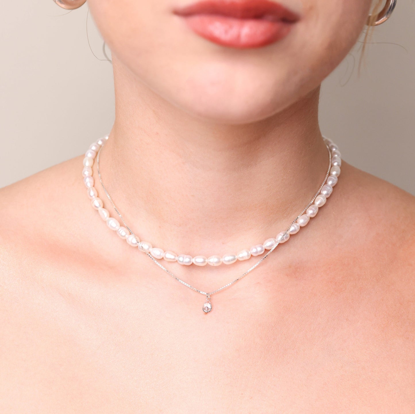 שרשרת ANNA כסף עדינה עם תליון טיפה נוצץ, על צוואר דוגמנית בשילוב שרשרת פנינים.
