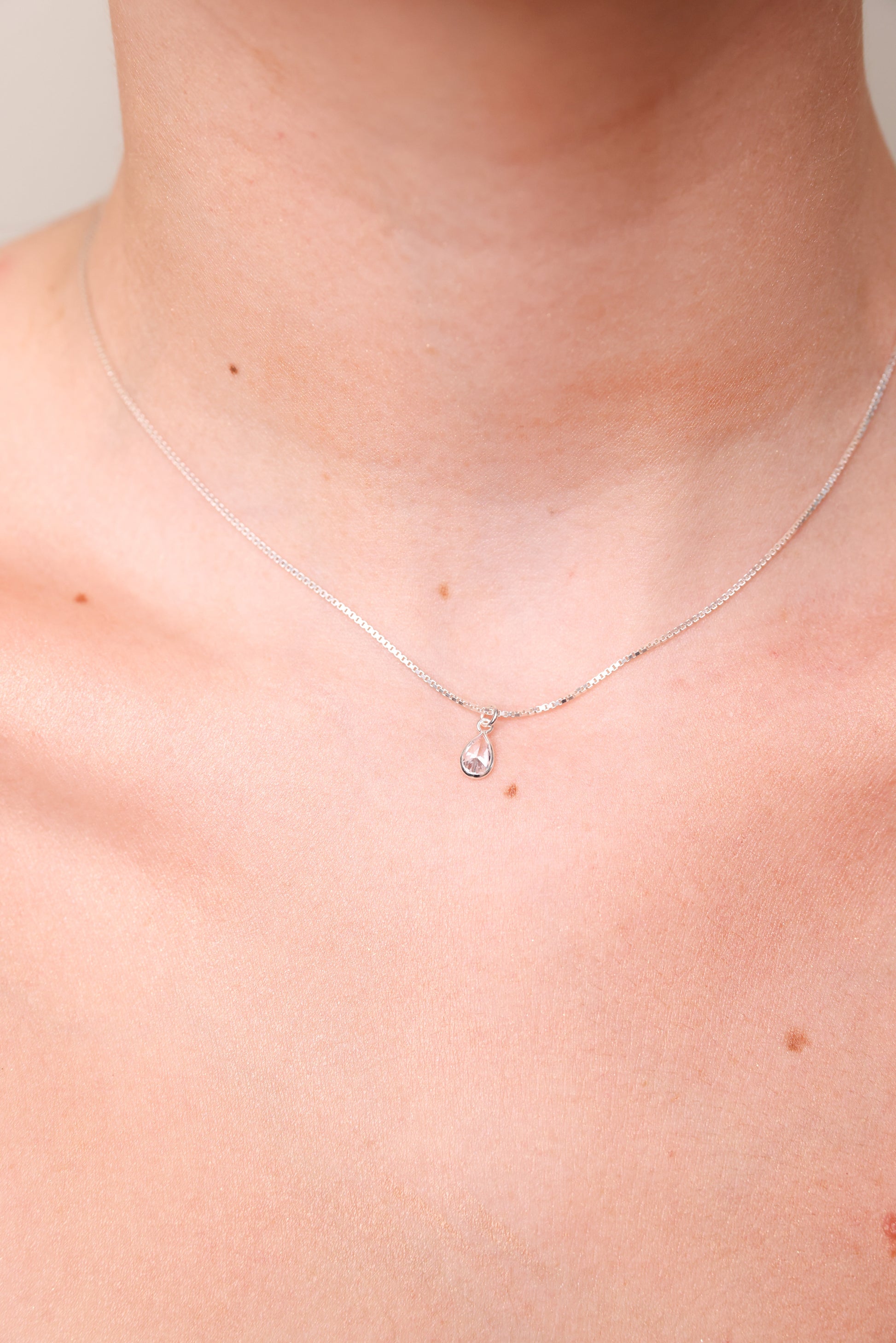 מבט תקריב על צוואר דוגמנית עונדת שרשרת DARIA NECKLACE כסף עם תליון טיפה שקוף.