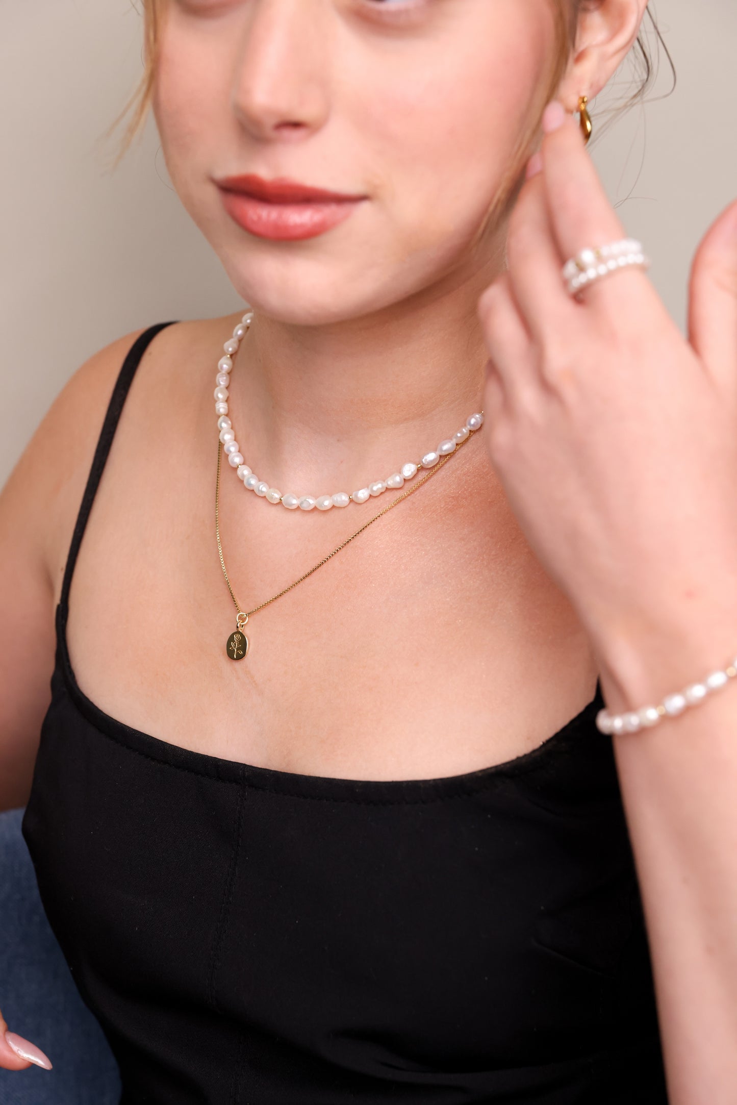 שרשרת BELA NECKLACE GOLD עדינה מזהב עם תליון ורד, משולבת בשרשרת פנינים על צוואר דוגמנית בטופ שחור. מבט תקריב.