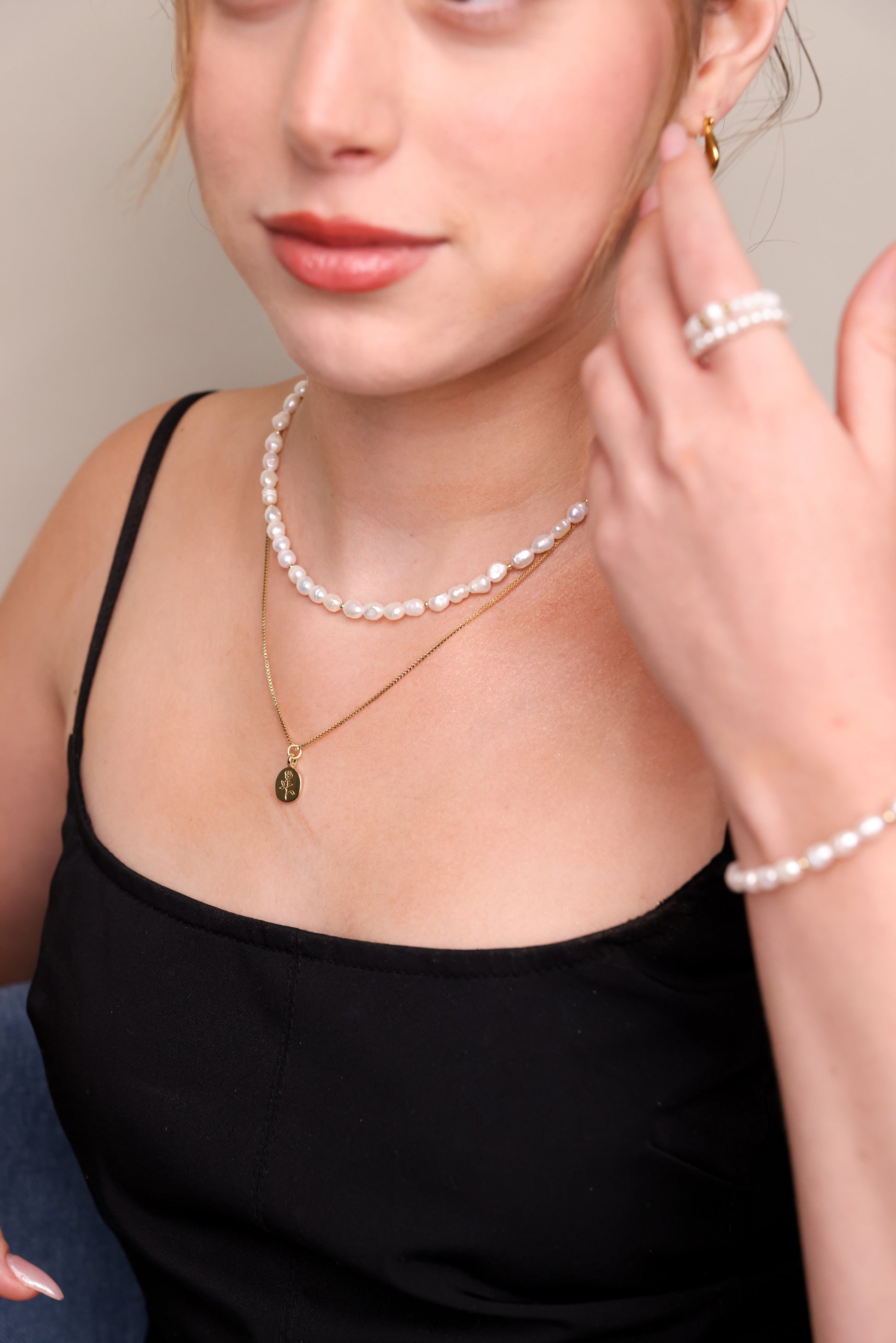 שרשרת BELA NECKLACE GOLD עדינה מזהב עם תליון ורד, משולבת בשרשרת פנינים על צוואר דוגמנית בטופ שחור. מבט תקריב.