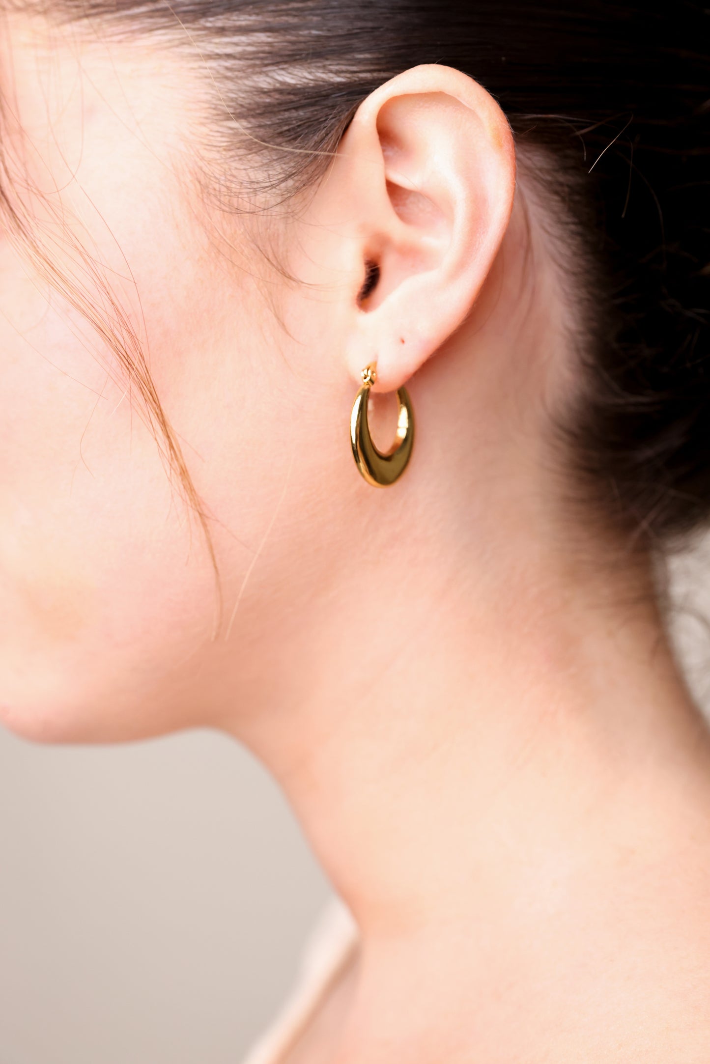 עגילי ÉLENA זהב על אוזן דוגמנית, תקריב פרופיל של עגיל חישוק אובלי עבה ובוהק.