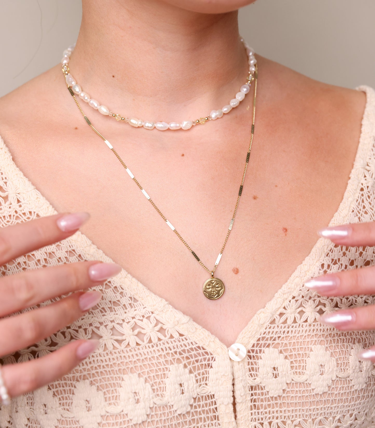 שרשרת ALAMOR YELLOW GOLD עם תליון פנים על חזה דוגמנית. מעליה צ'וקר פנינים וידיה מונחות על חולצת תחרה. מבט תקריב.