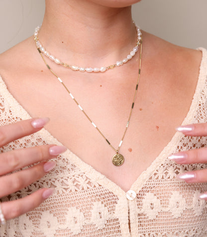 שרשרת ALAMOR YELLOW GOLD עם תליון פנים על חזה דוגמנית. מעליה צ'וקר פנינים וידיה מונחות על חולצת תחרה. מבט תקריב.