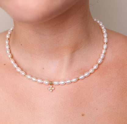 שרשרת NOA NECKLACE GOLD פנינים אליפטיות וזהב על צוואר דוגמנית, תקריב על תליון פרח מפנינים קטנות ואבן.