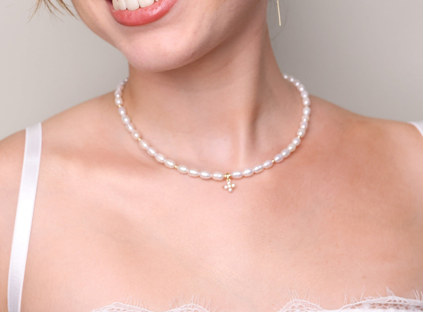 שרשרת NOA NECKLACE GOLD על צוואר דוגמנית מחייכת, עשויה פניני אורז, חרוזי זהב ותליון פרחוני. צילום קרוב.