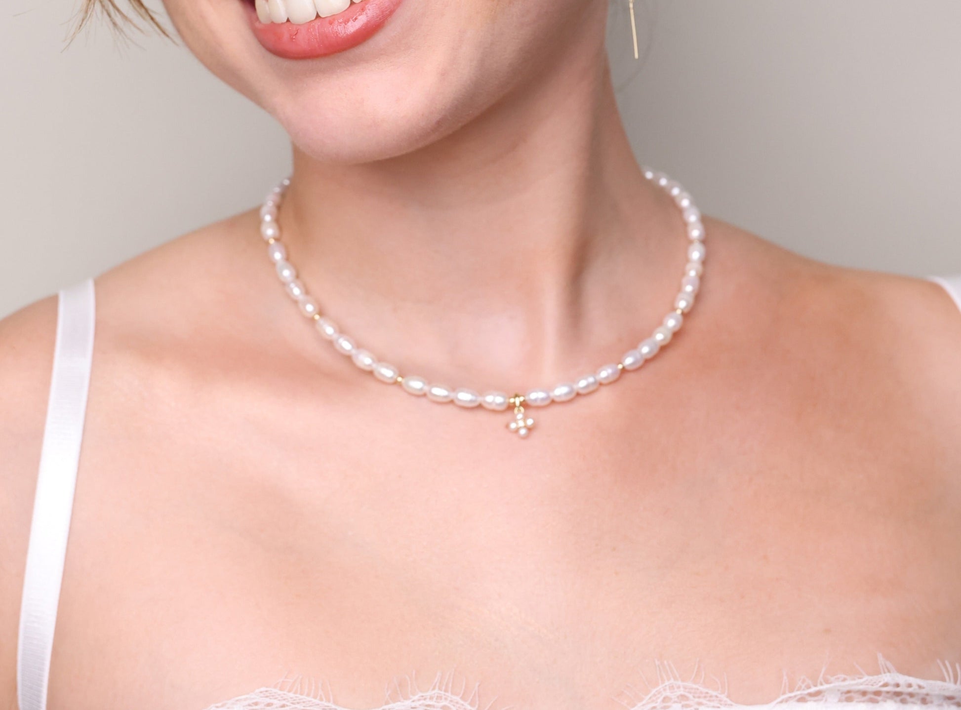 שרשרת NOA NECKLACE GOLD על צוואר דוגמנית מחייכת, עשויה פניני אורז, חרוזי זהב ותליון פרחוני. צילום קרוב.