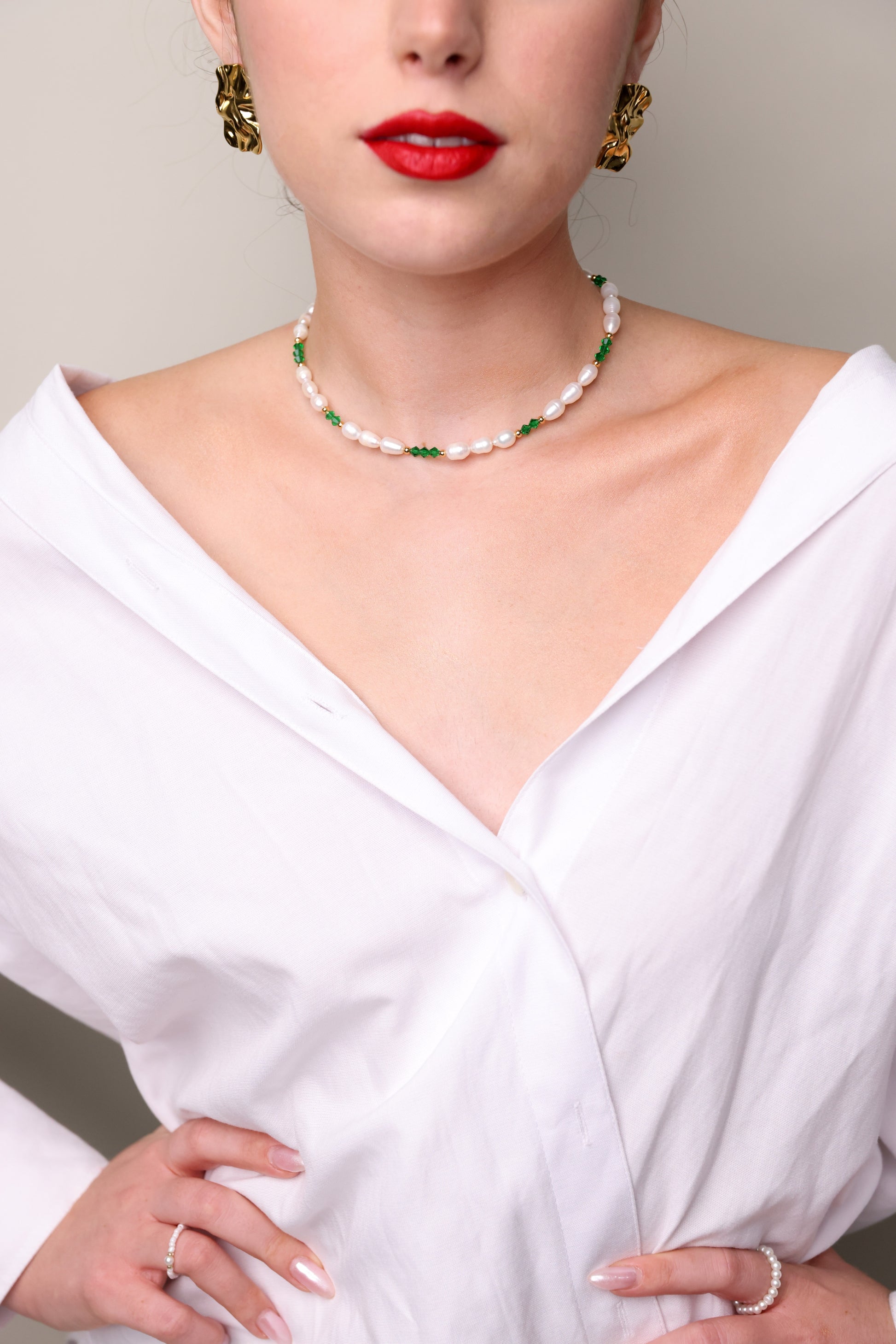 תקריב של שרשרת ALAMOR GREEN NECKLACE, פנינים ירוקות וזהב על צוואר דוגמנית בחולצה לבנה.