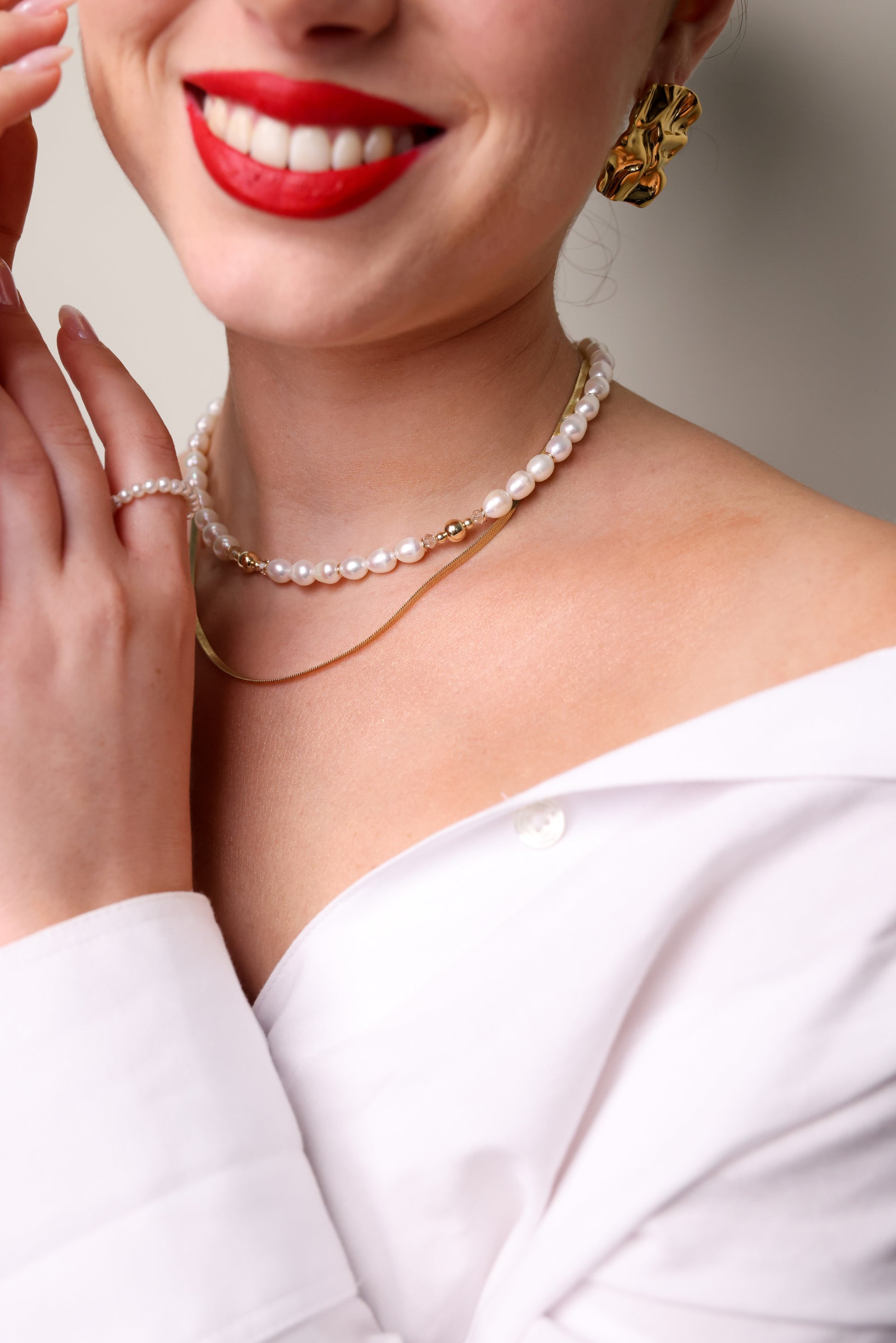 שרשרת ADIA שכבות (פנינים וזהב) על צוואר דוגמנית חייכנית, חולצה לבנה, עגיל זהב מפורט ויד עם טבעת פנינים.