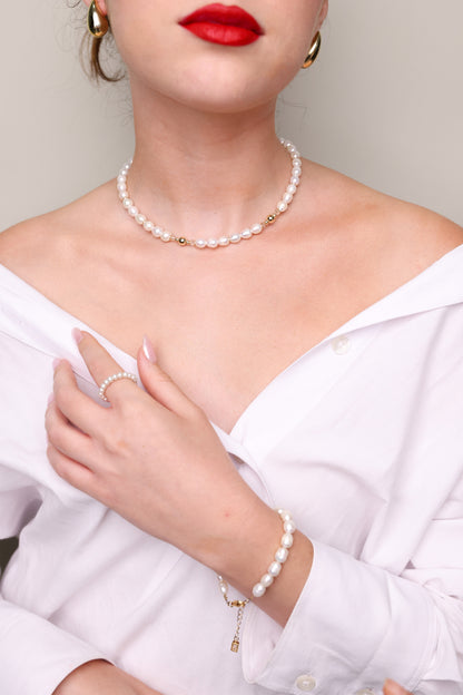 צמיד AMELIA BRACELET פנינים על פרק יד דוגמנית, בחולצה לבנה פתוחה, עם סוגר זהב ושרשרת פנינים.