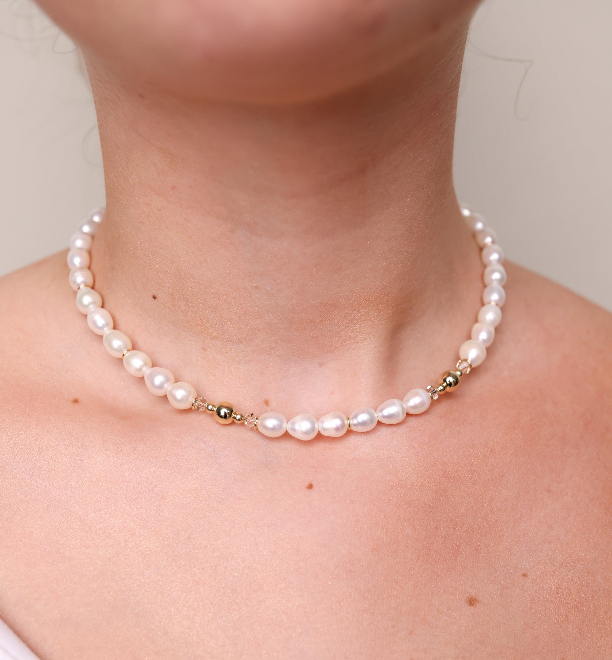 שרשרת קולר ADIA על צוואר דוגמנית, תקריב פניני מים מתוקים לבנות, חרוזי זהב וקריסטל זוהרים.