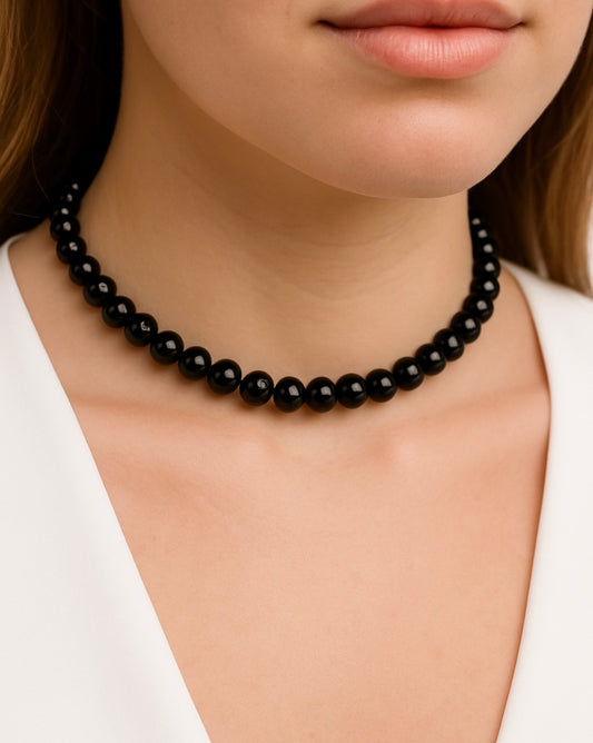 שרשרת ASA צמודה, חרוזים שחורים מבריקים על צוואר דוגמנית. תקריב של העיצוב על רקע חולצה לבנה.