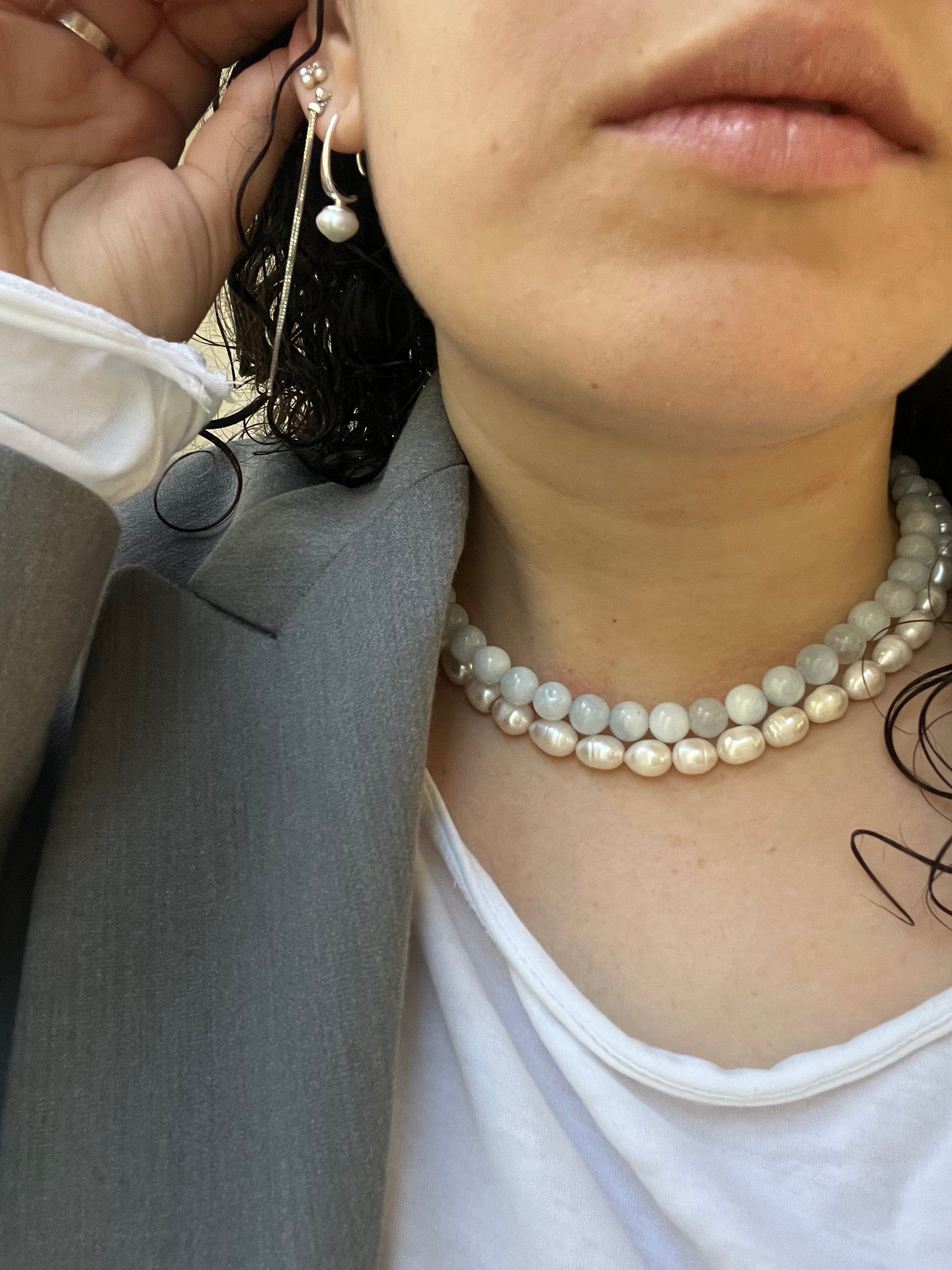 שרשרת ANGEL NECKLACE כפולה של Lidi: פנינים עגולות בהירות ופניני בארוק, על צוואר דוגמנית עם ז'קט אפור.