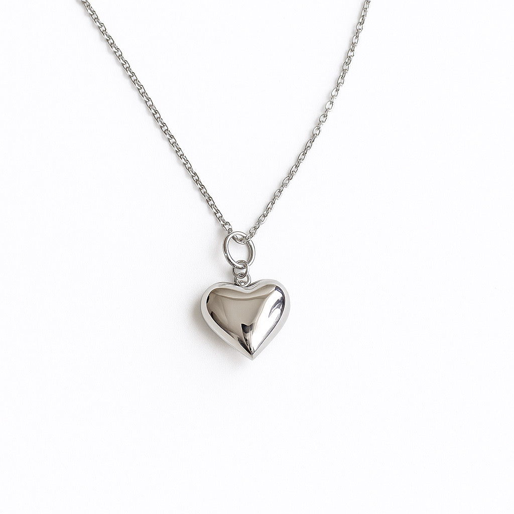 שרשרת FAT LOVE SILVER NECKALCE כסף, תליון לב מבריק ונפוח, מצולם מלמעלה על רקע לבן, פרטי השרשרת העדינה.