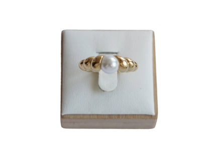 טבעת LOPE מזהב עם פנינה לבנה, בעלת פס גלי ייחודי, מוצגת מקדימה על סטנד.