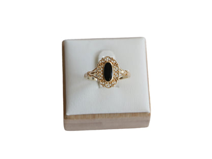 טבעת SOLE זהב עם אבן שחורה אובלית, מעוטרת במסגרת תחרה עדינה, מוצגת על סטנד לבן במבט קדמי.