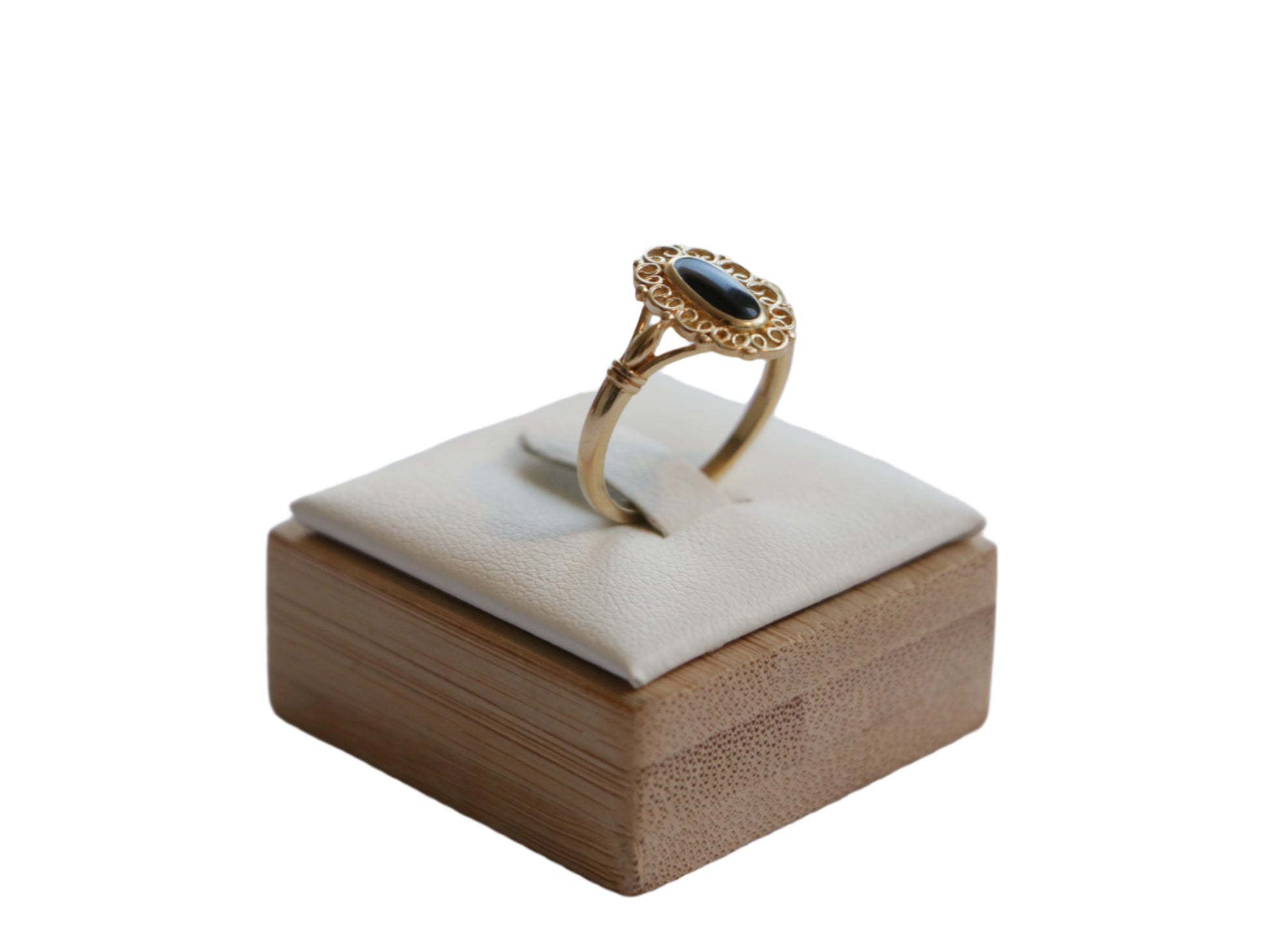 טבעת SOLE RING זהב עם אבן אובלית כהה ועיטור פילגרין, מבט צדדי על מעמד עץ מרופד.