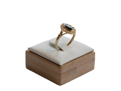 טבעת SOLE RING זהב עם אבן אובלית כהה ועיטור פילגרין, מבט צדדי על מעמד עץ מרופד.