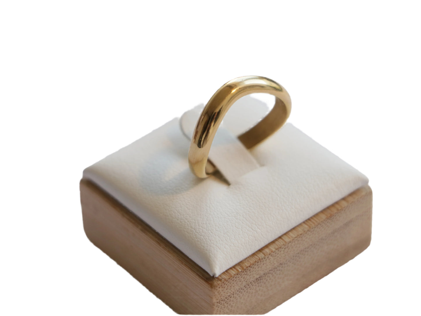 טבעת SKOP RING מזהב צהוב, מבריקה, מוצגת על סטנד דמוי עור לבן עם בסיס עץ, מצולמת מלמעלה קלות.