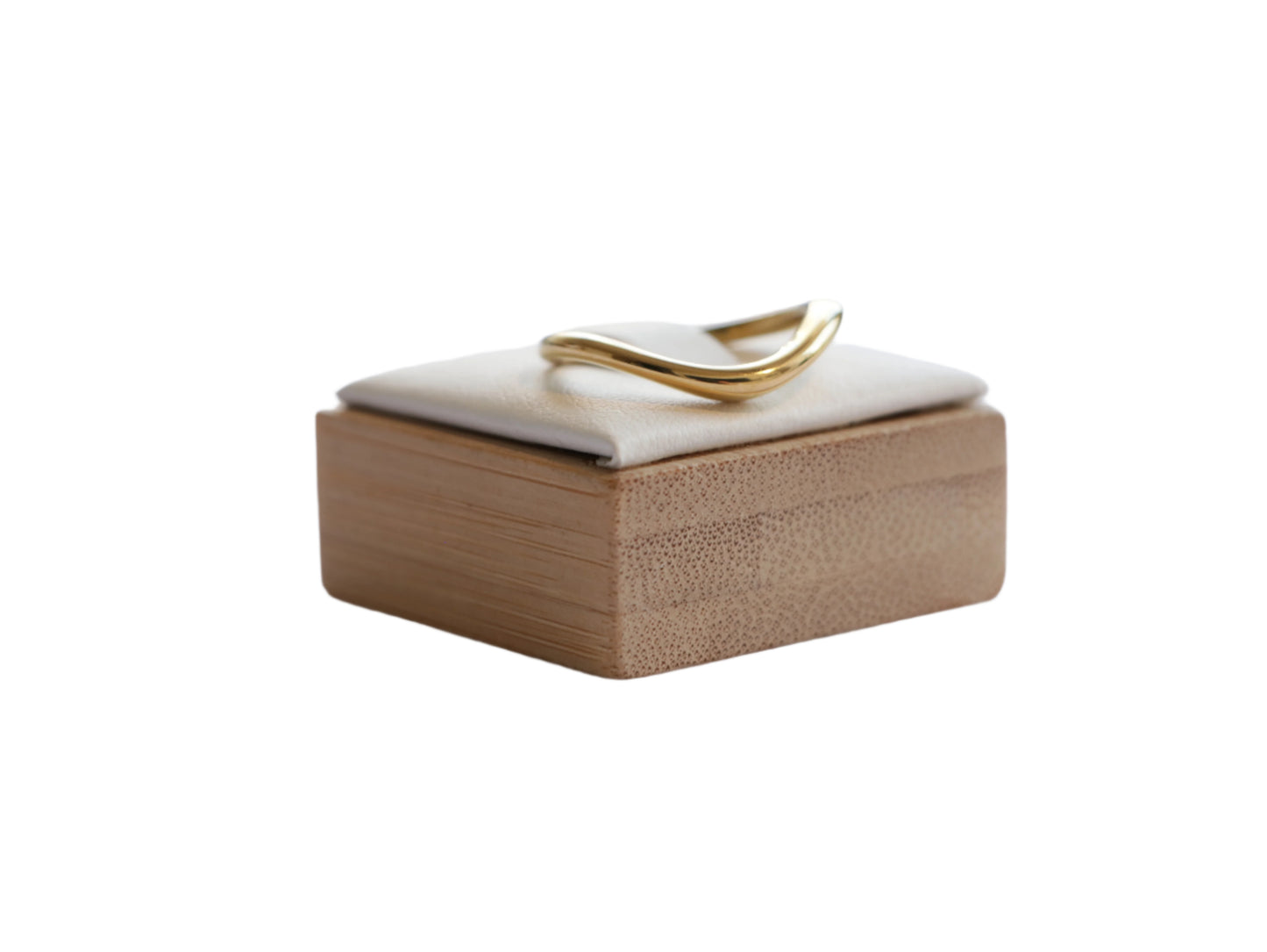 טבעת SKOP RING זהב בעיצוב גלי, מונחת על כרית בהירה בקופסת עץ עם טקסטורת שכבות. מבט צד.