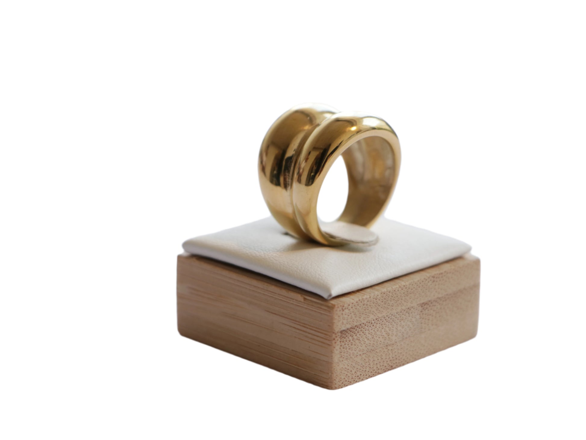 תקריב טבעת RAND RING מזהב, עיצוב גלי רחב ומבריק, על מעמד עץ וכרית לבנה.