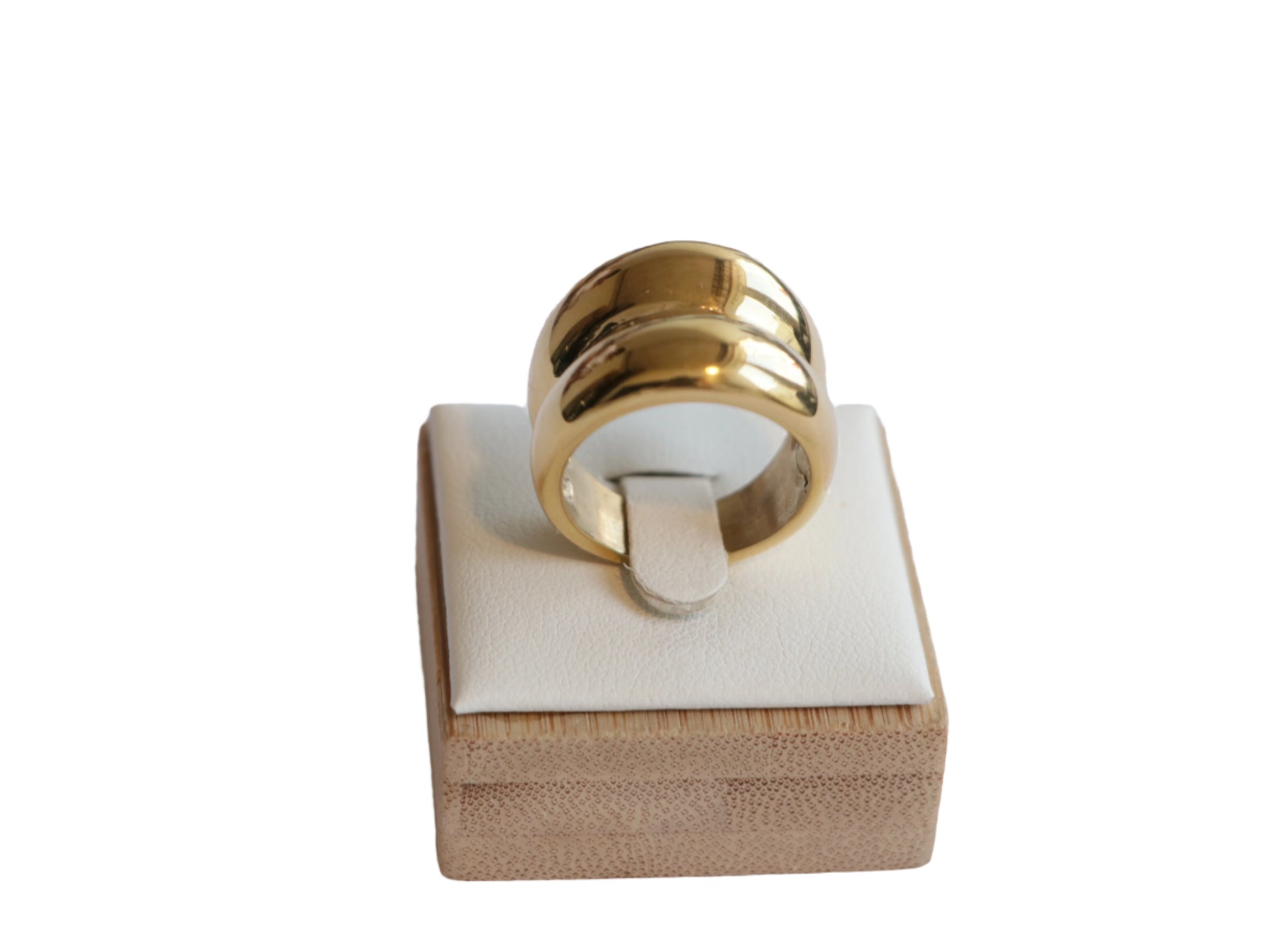 טבעת RAND זהב רחבה ומבריקה, מוצגת על סטנד תצוגה מעץ בהיר, זווית קדמית מוגבהת.