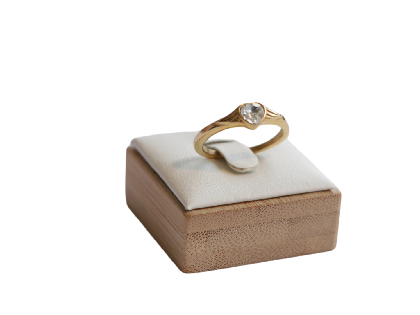תקריב של טבעת ZARK RING זהב עם אבן לב שקופה, מוצגת על סטנד עץ בהיר בזווית קדמית-צדית.