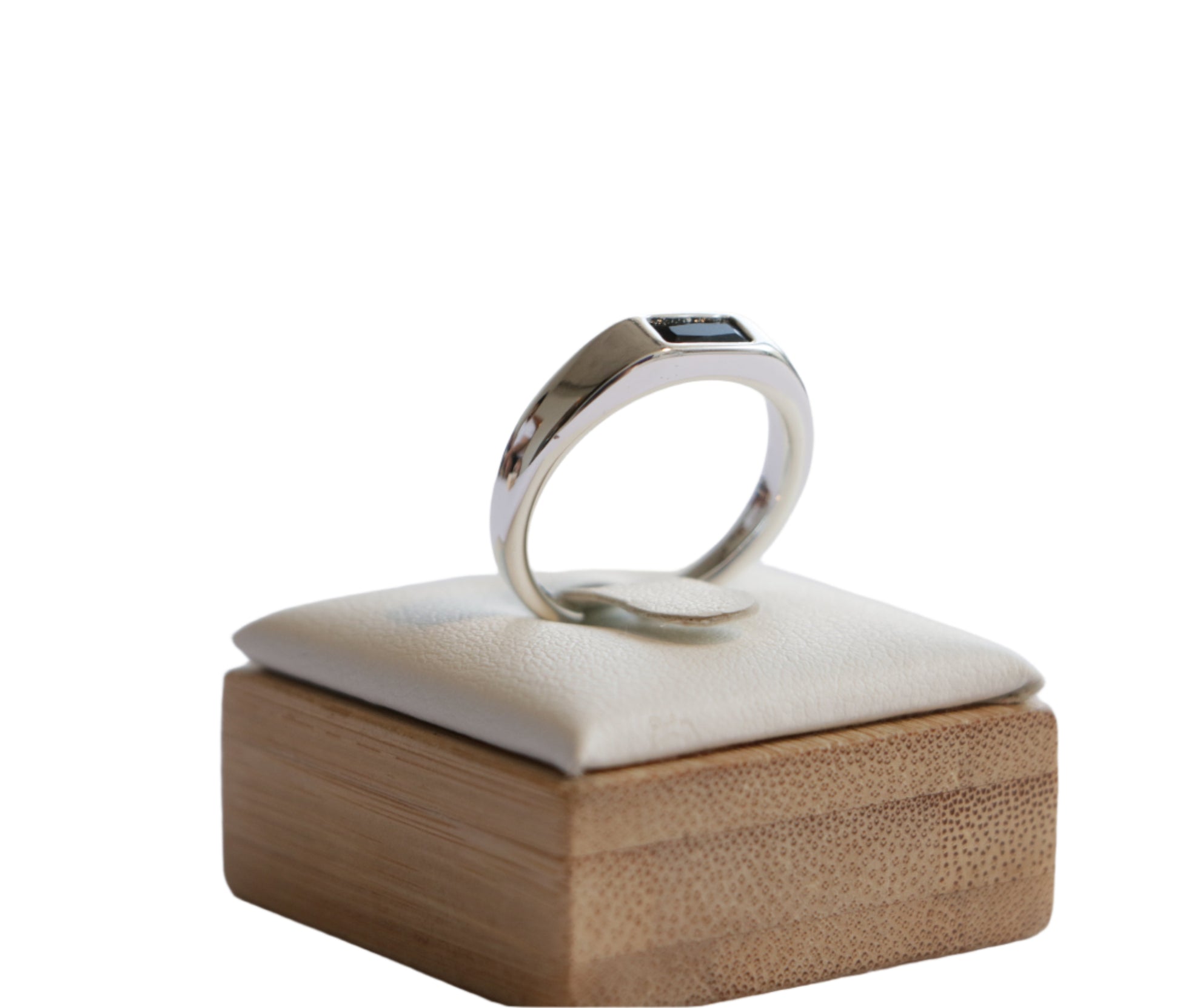 טבעת RAG RING מזהב לבן מלוטש, משובצת אבן מלבנית שחורה. מבט צד על סטנד עץ עם כרית בהירה.