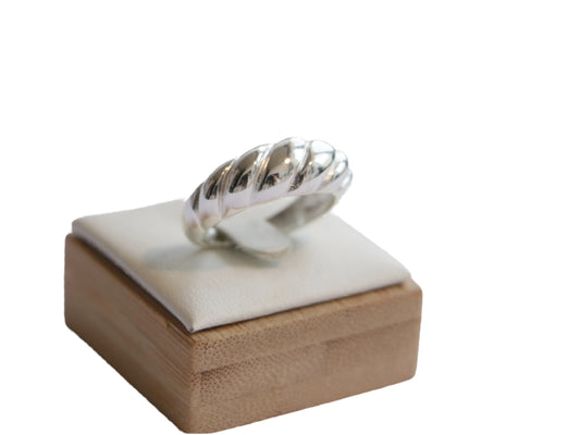 טבעת LAR RING כסף מבריקה עם פיתולים בולטים, מוצגת על מעמד מרופד עם בסיס עץ, מבט תקריב מלמעלה.