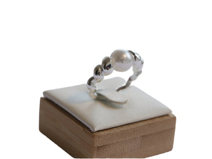 טבעת Lidi פנינה, פנינה מרכזית גדולה, מוקפת חרוזי כסף ופנינים קטנות. תקריב על מעמד עץ ולבן.