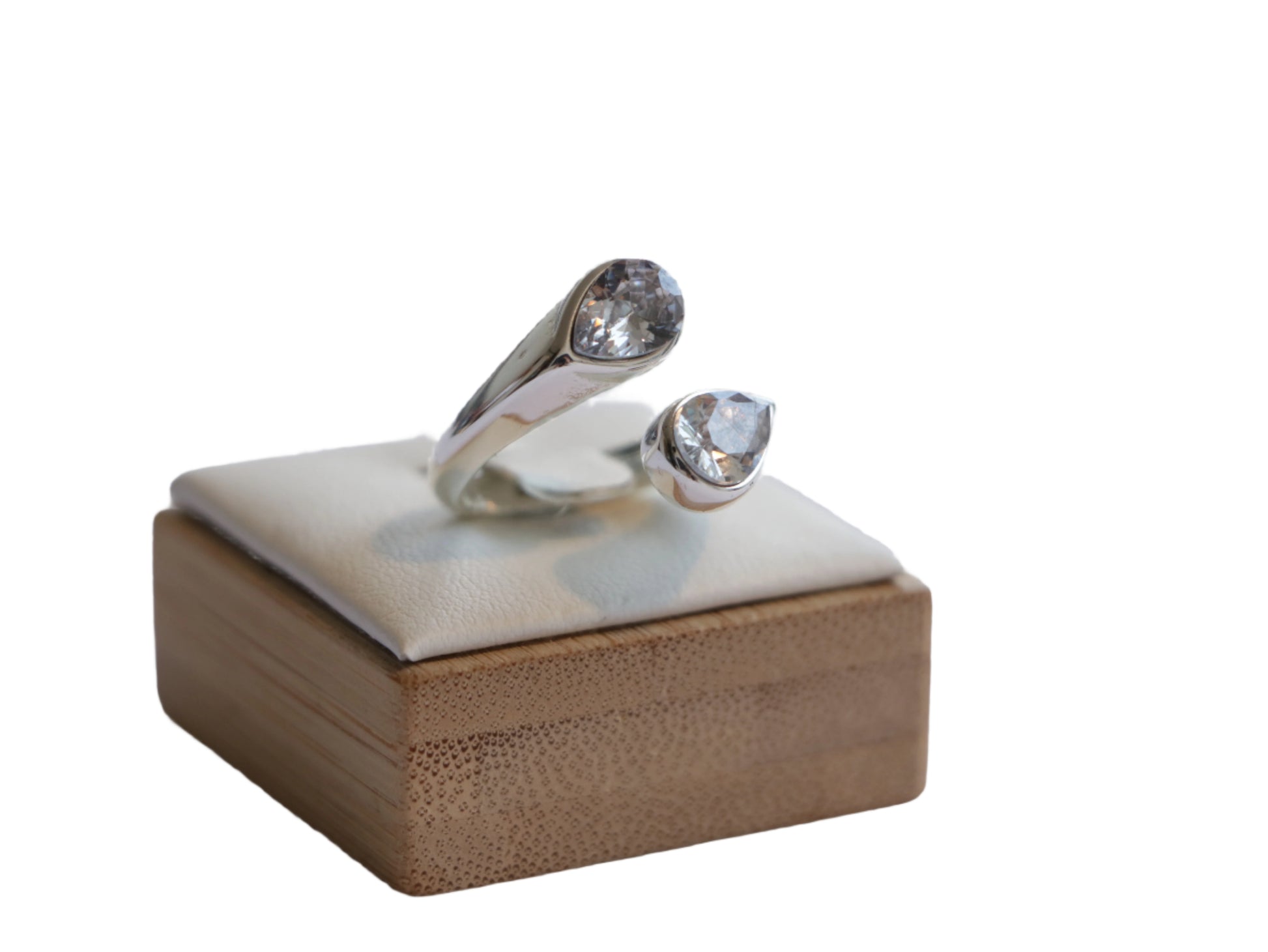 טבעת SHORE RING פתוחה בגוון כסף, משובצת בשתי אבנים נוצצות בגדלים שונים, על כרית תצוגה מעל עץ במבוק.