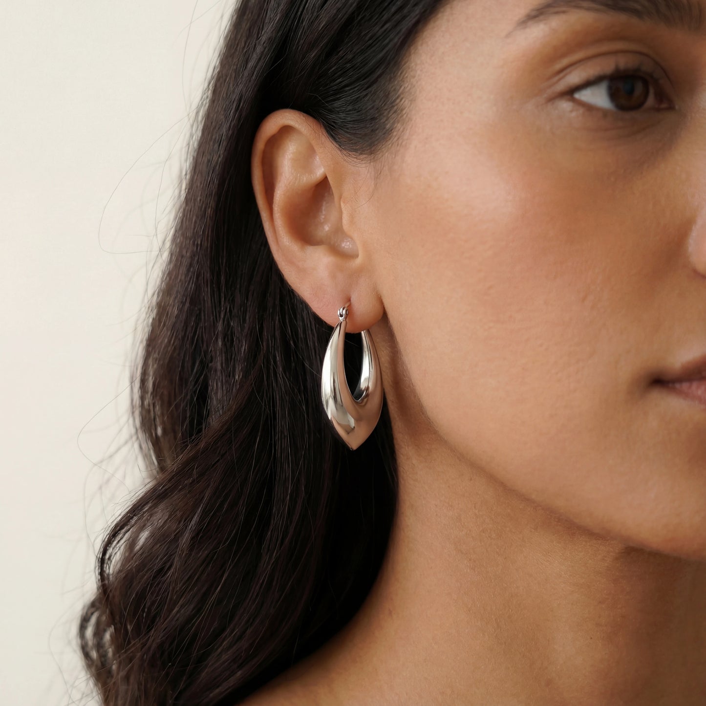 עגילי חישוק ALMOG ERRINGS SILVER יוקרתיים מסטיינלס סטיל בגוון כסף, מודגשים על אוזן אישה.