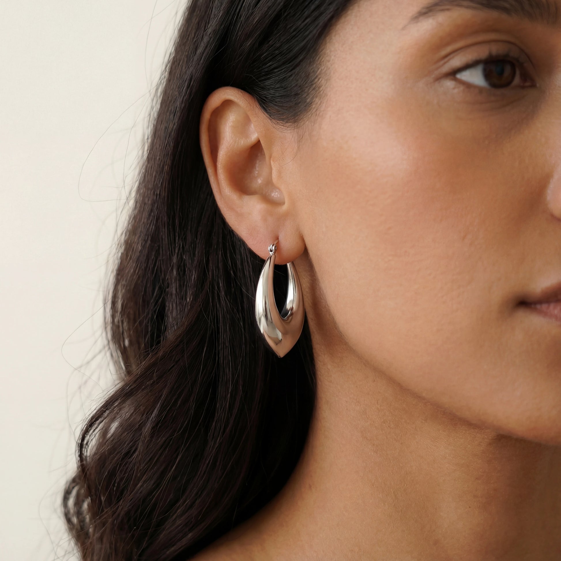 עגילי חישוק ALMOG ERRINGS SILVER יוקרתיים מסטיינלס סטיל בגוון כסף, מודגשים על אוזן אישה.