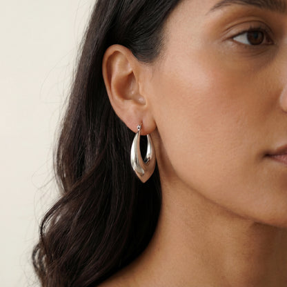 עגילי חישוק ALMOG ERRINGS SILVER יוקרתיים מסטיינלס סטיל בגוון כסף, מודגשים על אוזן אישה.