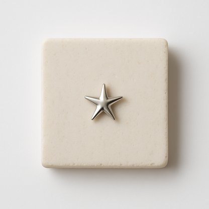 עגיל STAR EARRINGS בודד מכסף מבריק בצורת כוכב נפוח, מונח על משטח אבן בהיר מרובע, מבט תקריב.