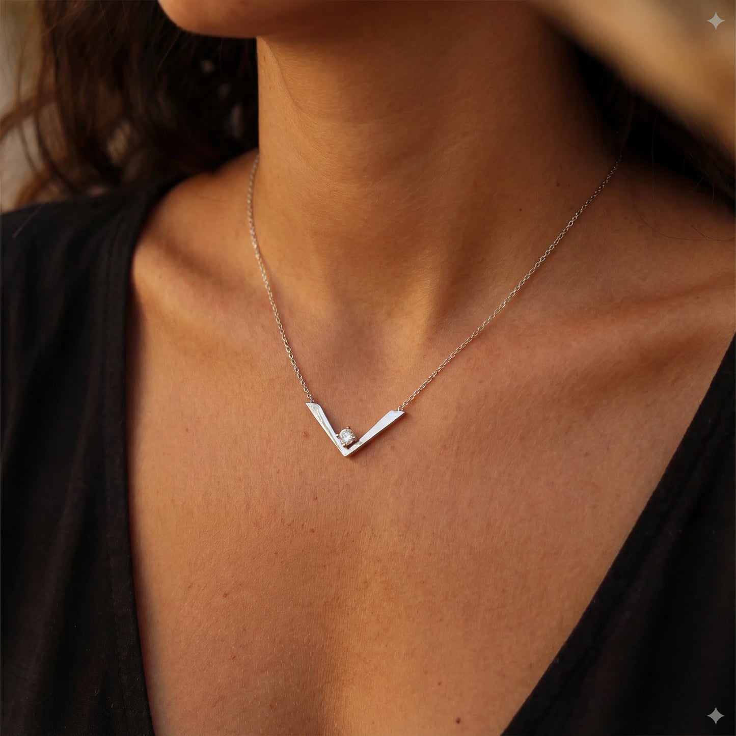 שרשרת GAYA NECKLACE יוקרתית מבית Lidi, עשויה סטיינלס סטיל עם תליון 'וי' משובץ זרקון נוצץ, על צוואר אישה.