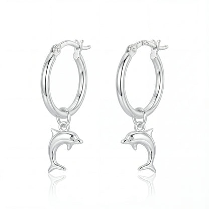 זוג עגילי חישוק מכסף 925 עם תליוני דולפין תלויים, מוארים באור עדין, על רקע כחול ימי. מותג Lidi.